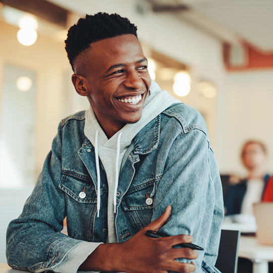 Student in a denim jacket sitting in a classroom smiling